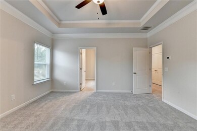 Unfurnished bedroom featuring a raised ceiling, ornamental molding, carpet flooring, and a ceiling fan