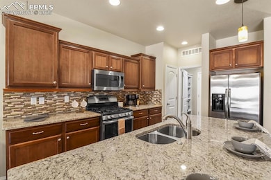 Kitchen featuring tasteful backsplash, visible vents, appliances with stainless steel finishes, light stone counters, and a sink