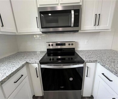 Kitchen with appliances with stainless steel finishes, white cabinetry, tasteful backsplash, and light stone countertops