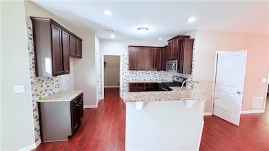 Kitchen with backsplash, a kitchen bar, dark brown cabinets, stainless steel appliances, and a peninsula