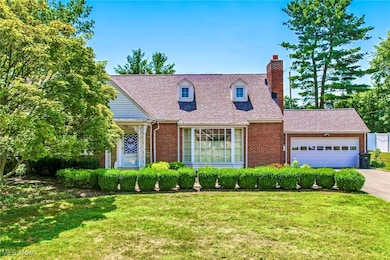 Cape cod home with a garage, a chimney, brick siding, and a front lawn
