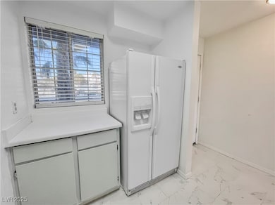 Kitchen with light countertops, white refrigerator with ice dispenser, marble finish floor, and baseboards