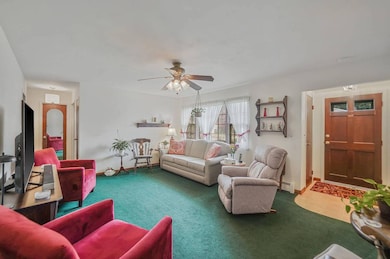 Carpeted living room featuring baseboard heating and a ceiling fan