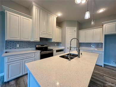 Kitchen with electric stove, an island with sink, white cabinetry, decorative backsplash, and decorative light fixtures