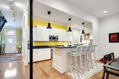 Kitchen featuring stainless steel microwave, dark countertops, a kitchen bar, light wood-style floors, and white cabinetry