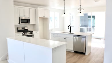 Kitchen with stainless steel appliances, white cabinetry, decorative light fixtures, and an island with sink