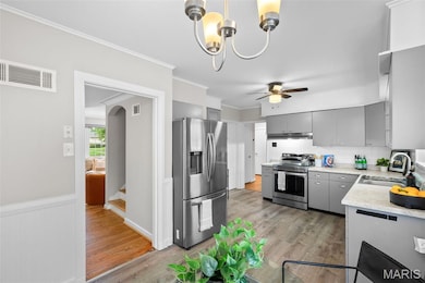 Kitchen featuring gray cabinets, light countertops, crown molding, tasteful backsplash, and appliances with stainless steel finishes