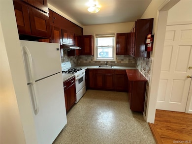 Kitchen with white appliances, light floors, backsplash, under cabinet range hood, and light countertops