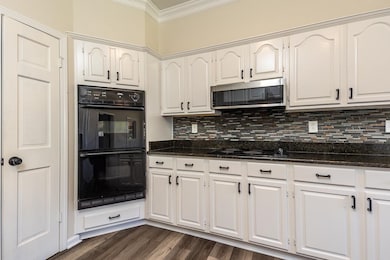 Kitchen featuring black appliances, dark stone counters, white cabinetry, dark wood-type flooring, and decorative backsplash