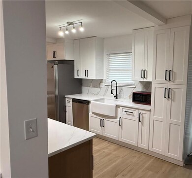 Kitchen featuring white cabinetry, light wood-type flooring, appliances with stainless steel finishes, decorative backsplash, and light stone counters