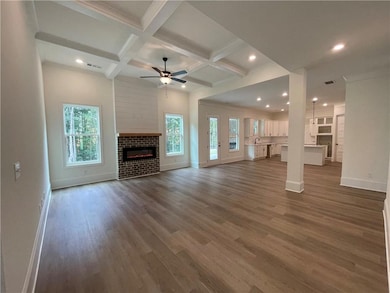 Unfurnished living room featuring coffered ceiling, a fireplace, plenty of natural light, a ceiling fan, and dark wood-type flooring