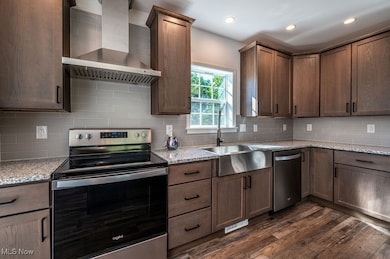 Kitchen with stainless steel appliances, wall chimney range hood, light stone countertops, dark wood finished floors, and tasteful backsplash