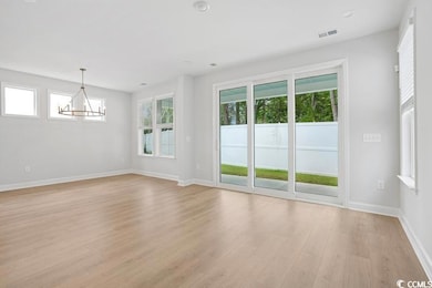 Spare room with a chandelier, light wood finished floors, and healthy amount of natural light