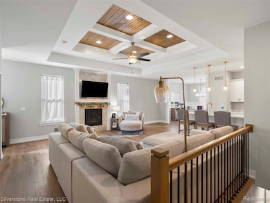 Living area featuring coffered ceiling, a wooden ceiling with exposed beams, light wood-type flooring, a tray ceiling, and a ceiling fan