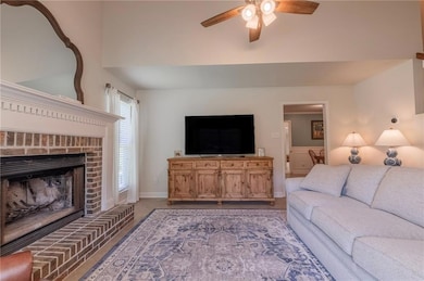 Carpeted living area with a ceiling fan and a brick fireplace