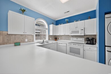 Kitchen with white cabinets, white appliances, crown molding, estacked washer and dryer, and light countertops