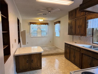 Kitchen featuring dark brown cabinets, a textured ceiling, a textured wall, light countertops, and a ceiling fan