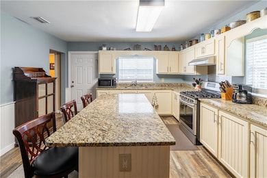 Kitchen with appliances with stainless steel finishes, light wood-style floors, a breakfast bar area, a center island, and under cabinet range hood