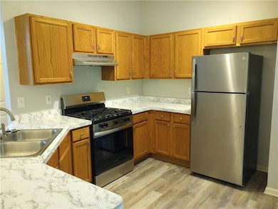 Kitchen featuring stainless steel appliances, light countertops, brown cabinetry, and under cabinet range hood