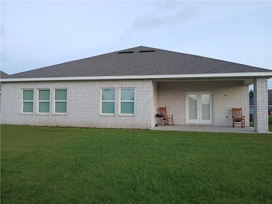 Rear view of property with brick siding, a yard, roof with shingles, and a patio