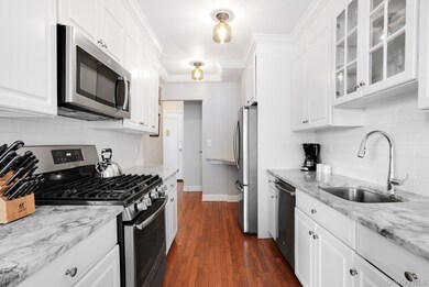 Kitchen with stainless steel appliances, granite counters, baseboards, white cabinetry, glass insert cabinets & hardwood flooring