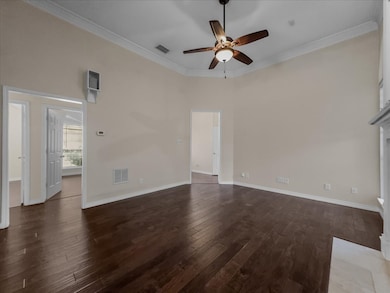 Unfurnished living room featuring ornamental molding, dark wood-type flooring, ceiling fan, and a high ceiling