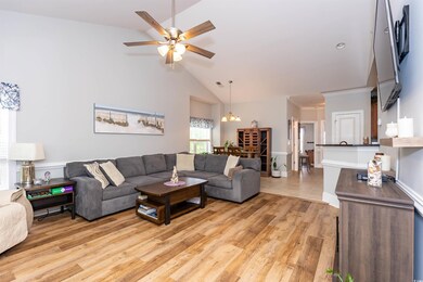 Living room featuring visible vents, high vaulted ceiling, ceiling fan with notable chandelier, and light wood finished floors