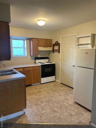 Kitchen with fridge, range with electric cooktop, light countertops, brown cabinets, and range hood