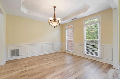 Unfurnished room featuring a tray ceiling, crown molding, a chandelier, light wood-type flooring, and a wainscoted wall