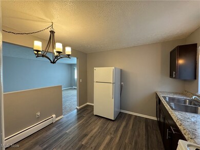 Kitchen with sink, a baseboard radiator, white fridge, dark brown cabinetry, and a chandelier