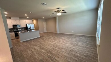 Kitchen featuring appliances with stainless steel finishes, white cabinets, ceiling fan, hardwood / wood-style flooring, and a center island with sink