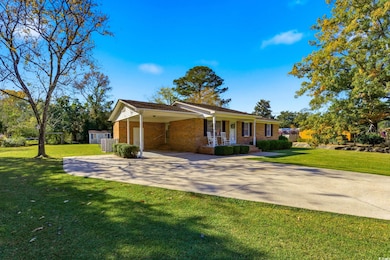 View of front of house with a front lawn, driveway, a porch, a carport, and brick siding