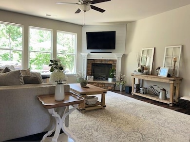Living room featuring ceiling fan, plenty of natural light, wood finished floors, and a stone fireplace
