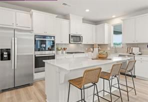 Kitchen with appliances with stainless steel finishes, light wood finished floors, white cabinetry, a center island, and recessed lighting
