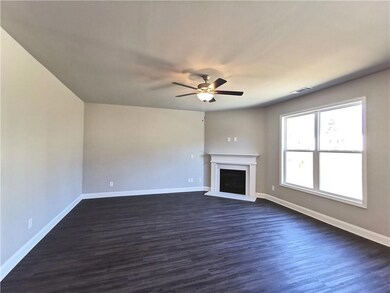 Unfurnished living room with ceiling fan, a fireplace with raised hearth, and dark wood-style flooring