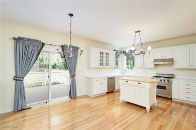 Kitchen featuring a chandelier, light countertops, stainless steel appliances, glass insert cabinets, and pendant lighting