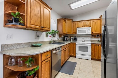 Kitchen featuring open shelves, white appliances, vaulted ceiling, light tile patterned floors, and brown cabinetry