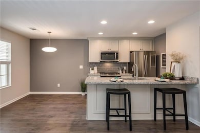 Kitchen with tasteful backsplash, light stone counters, appliances with stainless steel finishes, a breakfast bar, and a peninsula