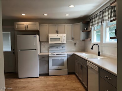 Kitchen featuring gray cabinetry, white appliances, light countertops, open shelves, and decorative backsplash