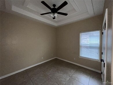 Empty room featuring a raised ceiling, ceiling fan, baseboards, and tile patterned floors