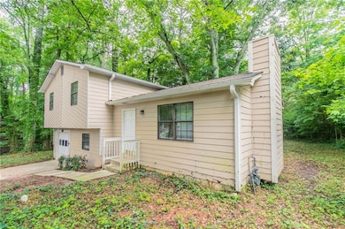 Tri-level home with a chimney, a garage, concrete driveway, and view of scattered trees