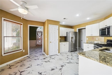 Kitchen featuring light stone counters, stainless steel appliances, white cabinetry, light marble finish floors, and recessed lighting