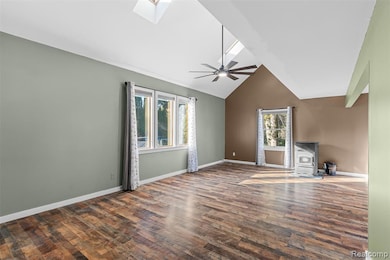 Unfurnished living room with a wood stove, a skylight, healthy amount of natural light, dark wood-type flooring, and high vaulted ceiling