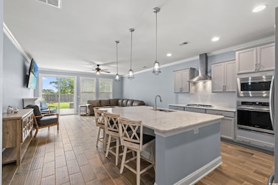Kitchen featuring tasteful backsplash, gray cabinetry, open floor plan, hanging light fixtures, and crown molding