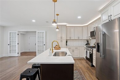 Kitchen with appliances with stainless steel finishes, a kitchen island with sink, light wood-type flooring, tasteful backsplash, and pendant lighting