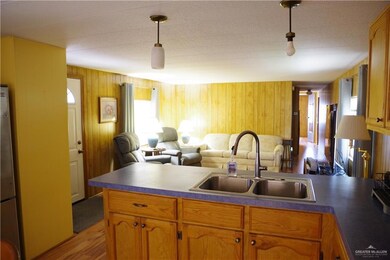 Kitchen featuring a peninsula, a sink, light wood finished floors, dark countertops, and pendant lighting