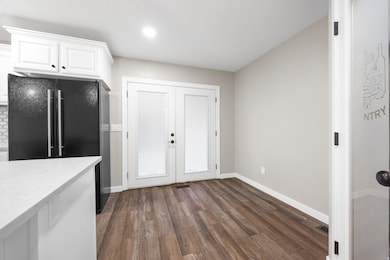 Kitchen with dark wood finished floors, white cabinets, light stone counters, black fridge, and french doors