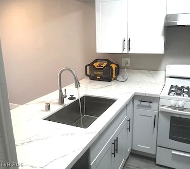 Kitchen with white gas stove, light stone countertops, wall chimney exhaust hood, and gray cabinets