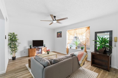 Living room with a textured ceiling, ceiling fan, light wood-style floors, and ornamental molding