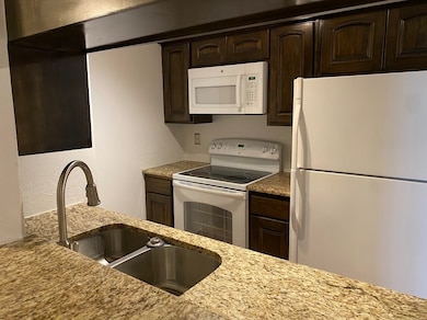 Kitchen featuring dark brown cabinetry, granite countertops, and white appliances